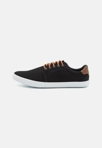 Zapatillas de lona negras con suela de goma blanca, detalles de cuero marrón, seis ojales con cordones marrones y un diseño aerodinámico.