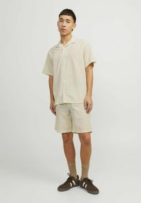 Kortærmet skjorte med krave og matchende shorts i lys beige med ribbet tekstur og subtile lodrette striber. Brune sneakers og brune sokker.