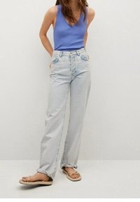 Jasnoniebieskie dżinsy o luźnym kroju i wysokim stanie, zestawione z niebieską koszulką na ramiączkach i beżowymi klapkami.