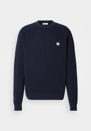 Pulover tricotat de culoare albastru marin, cu o textură cordată, guler rotund și patch cu logo pe partea stângă a pieptului. Mansete și tiv ajustate.