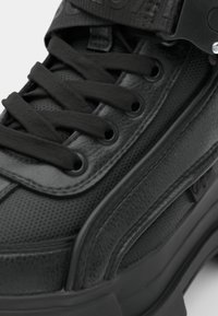 Black sneaker with textured leather and mesh upper, featuring thick black laces, side straps, and a chunky rubber sole.