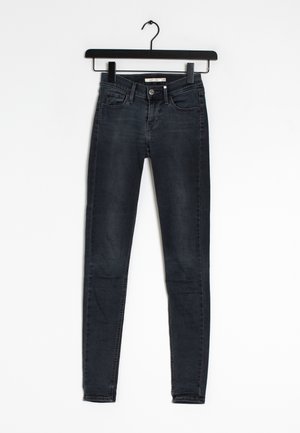 Jean skinny noir en denim, présentant un design classique à cinq poches et des passants de ceinture, suspendu à un cintre en plastique noir.