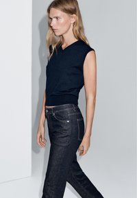 Top senza maniche blu navy con scollo a V abbinato a jeans in denim scuro con cuciture dorate e design classico a cinque tasche.