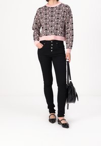 Jeans negros de cintura alta con un cierre frontal de cinco botones, combinados con un suéter de patrón de corazones en rosa y negro y zapatos planos negros.