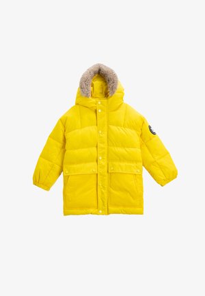 Chaqueta acolchada amarilla con capucha forrada de piel sintética, cierres de presión, dos bolsillos delanteros y puños elásticos. Diseño acolchado en toda la prenda.