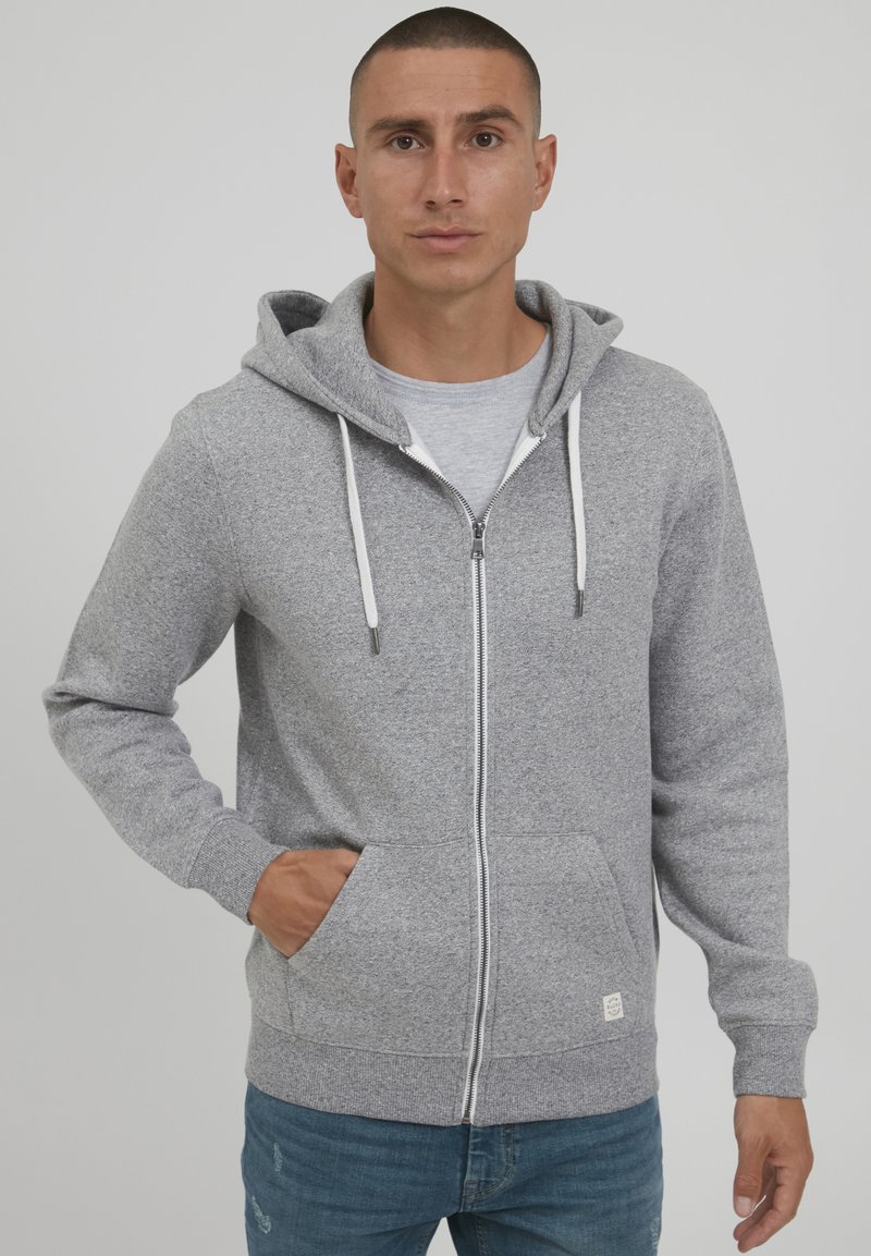 Sivi zip-up dukserica od teksturiranog materijala, s prednjim džepom, podesivom kapuljačom s vezicom, te rebrastim manžetama i donjim rubom.