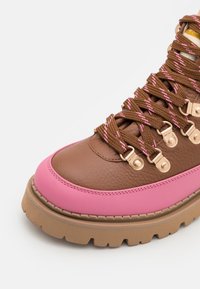 Brune lædersneaker med pink gummidetaljer, rund tå, struktureret overflade, og brune samt pink snørebånd, der har metalliske øskner og en kraftig sål.