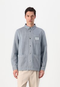 Casaco riscado masculino em azul claro e branco, feito de algodão. Apresenta um fecho frontal com botões, gola e dois bolsos frontais.
