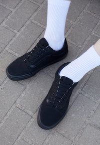 Sneakers neri in tela con lacci neri e suole in gomma. Indossati con calze bianche a coste, caratterizzate da un design semplice e profilo piatto.