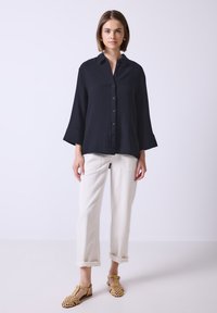 Marinblå button-up skjorta med klockärmar, strukturerad tyg; kombinerad med uppkavlade krämfärgade byxor och vävda bruna sandaler.