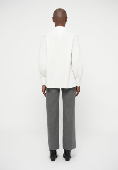 Hvid langærmet bluse med samlede pufærmer, parret med grå bredbenede bukser. Sorte ankelstøvler fuldender sættet.