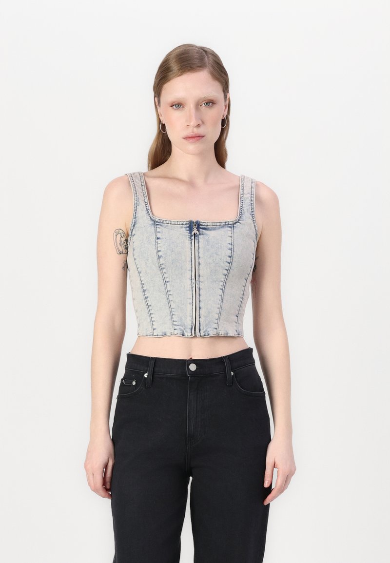 Top in denim blu chiaro, corto, con scollatura quadrata e cerniera centrale, caratterizzato da cuciture verticali e spalline larghe. Abbinato a pantaloni neri.