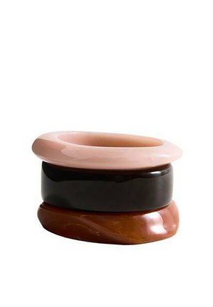 Tri naskladané hladké, lesklé náramky v svetlo ružovej, čiernej a mramorovo hnedej farbe na bielom pozadí.