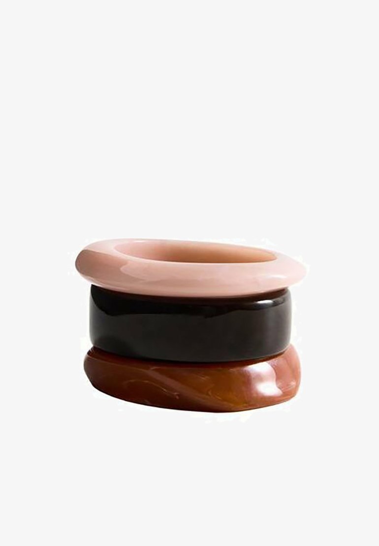 Trois bracelets lisses et brillants empilés, en rose clair, noir et marron marbré, sur un fond blanc.