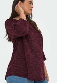 Top a maniche lunghe bordeaux con texture, vestibilità ampia, maniche 3/4 e orlo arrotondato, abbinato a jeans blu.