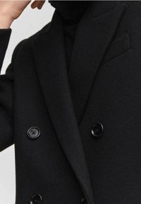 Sort dobbeltradet blazer lavet af tekstureret stof, med spidse klapper, sidelommer og blanke sorte knapper.