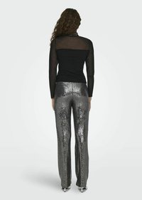 Schwarzes Langarmshirt mit transparenten Einsätzen, kombiniert mit silbernen Pailletten-Hosen, die einen geraden Schnitt und eine glänzende Textur aufweisen.
