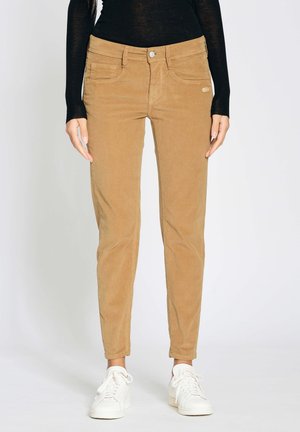 Beige Cordhosen in schlanker Passform, mit Fronttaschen, Knopfverschluss und glatter Textur. Kombiniert mit weißen Sneakern.