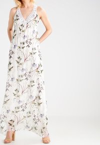 Robe maxi en tissu léger blanc avec un imprimé floral aux couleurs douces. Détails comprenant un décolleté en V et des accents délicats en dentelle.