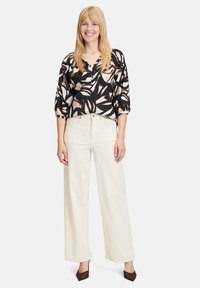 Blusa a fantasia nera e crema con maniche 3/4, abbinata a pantaloni larghi crema. Scarpe con tacco marroni completano l'outfit.