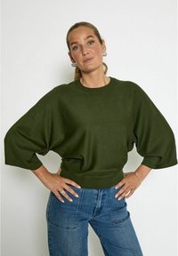 Pull en tricot vert avec une coupe large et décontractée, et des manches aux coudes. Présente un ourlet côtelé et un tissu doux et texturé. Assorti à un jean en denim.