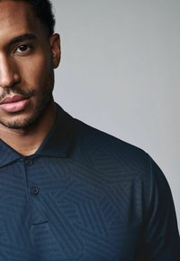 Mørkeblå polo shirt med et struktureret geometrisk mønster, tre-knaps lukning og en kort krave, der fremhæver subtile syninger.
