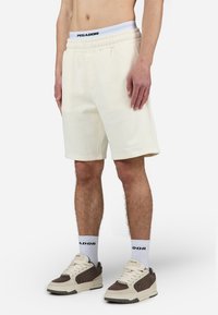 Cremefarvede shorts med elastisk talje, diskret logo detalje, lige ben design og blød tekstur, parret med neutralt farvede sneakers.