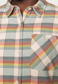 Button-up shirt featuring a multi-colored plaid pattern with red, green, and yellow accents. Includes a chest pocket and soft fabric texture.