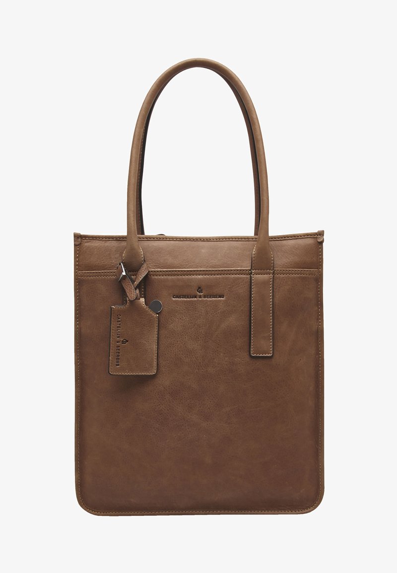 Braune Leder-Tote-Tasche mit glatter Textur, zwei oberen Griffen, einer Fronttasche und einem angehängten Gepäckanhänger. Subtile Nahtdetails sichtbar.