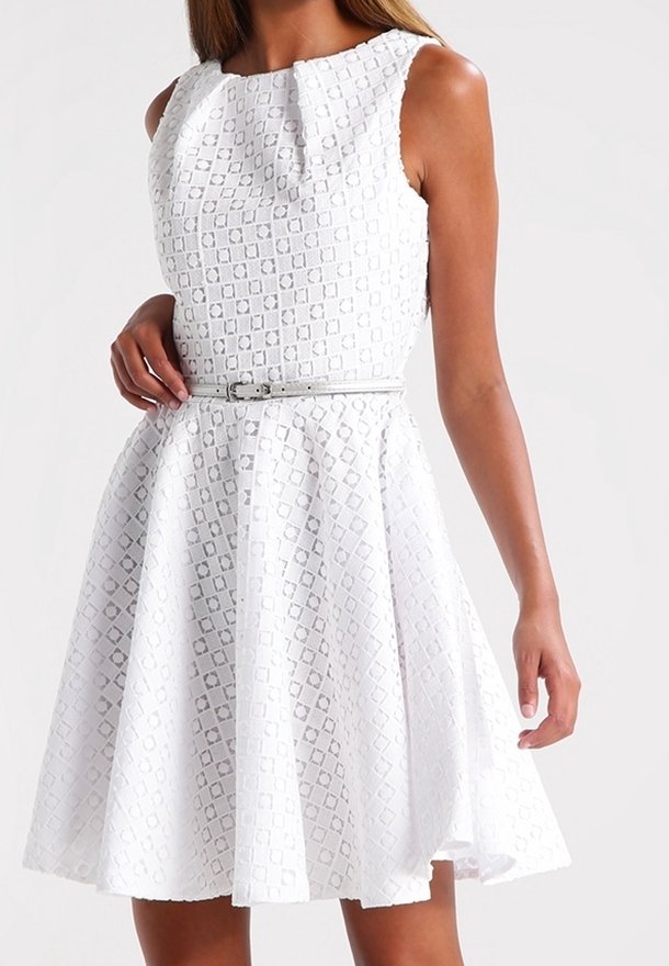 Robe blanche sans manches avec motif carré texturé, taille cintrée avec une fine ceinture et jupe évasée en ligne A portée par une personne.