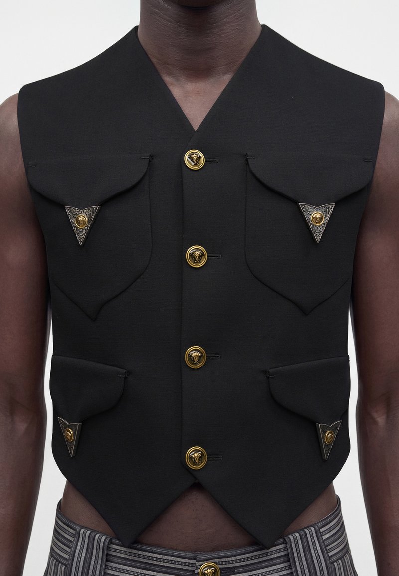 Gilet sans manches noir avec quatre boutons dorés et quatre poches à rabat, chaque poche sécurisée par un bouton décoratif triangulaire.