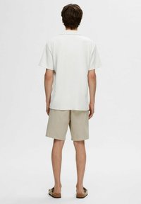 Hvit kortermet skjorte med krage, kombinert med beige shorts. Skjorten har et strukturert stoff, mens shortsen er glatt med rett snitt.