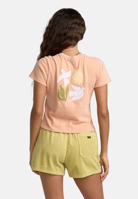Kortærmet lyserød bomulds t-shirt med hvide blomster- og solgrafikker, parret med gule corduroy-shorts med baglomme.