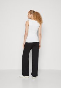White sleeveless top paired with black wide-leg pants, featuring a smooth texture and a relaxed fit, set against a plain white background.