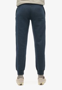Marineblauwe trainingsbroek met een tapse pasvorm, elastische boorden en een achterzak. Textuurstof en casual fit. Draag met lichtgekleurde schoenen.