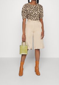 Tričko s krátkým rukávem v leopardím vzoru, béžové šortky s vysokým pasem, hnědé kozačky na podpatku a malá zelená kabelka s krokodýlovou texturou.