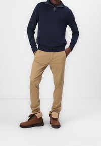 Marinblå zip-hals-tröja, beige slim-fit byxor och bruna ankelskor med pälsfoder och snören. Enkelt, rent design med neutral färgpalett.