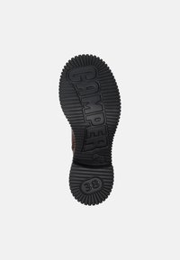 Suela de zapato de goma negra con textura acanalada, con el logo "CAMPER" y la talla "38" en relieve sobre la superficie, diseñada para ofrecer agarre y durabilidad.
