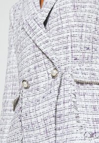 Blazer en tweed texturé violet clair et blanc avec des boutons ornés de perles et des bords effilochés aux poches et aux revers.