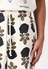 Hvite stoffbukser med et dristig blomster mønster i svart med brune blader, elastisk livlinje og snor for justerbar passform.