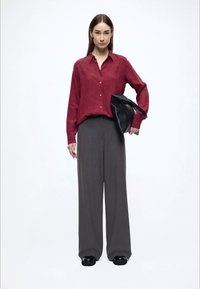 Red button-up shirt with a fine texture, high-waisted gray trousers, and a black handbag, worn with black slip-on shoes.