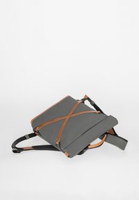 Grau Stoff-Rucksack mit braunen Lederakzenten, flachem Design, verstellbaren Trägern und einem markanten Kreuzgurt-Detail an der Vorderseite.