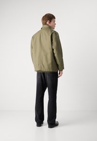 Olive green, collar jacket with a clean design, featuring long sleeves and a relaxed fit, paired with black denim pants and shoes.