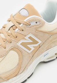 Baskets en suède beige et textile crème avec un logo "N" blanc bien visible, des accents texturés et des lacets beiges sur une semelle amortissante.