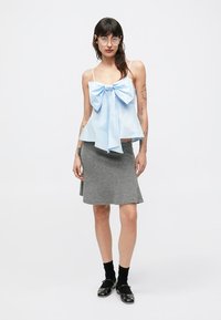 Jasnoniebieski krótki top z dużą kokardą z przodu, zestawiony z szarą rozkloszowaną spódnicą. Modelka ma na sobie czarne chodaki i wysokie skarpety do kolan.