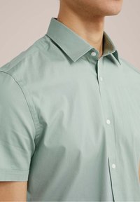 Ljusgrön kortärmad skjorta i mjuk bomull med krage som knäpps, med en rad vita knappar längs placket.