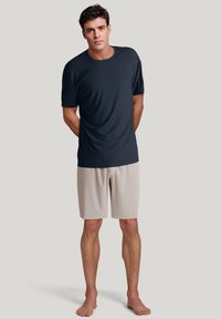 Marineblauw korte mouw shirt met een gladde textuur, gecombineerd met lichte shorts met een patroon van diamanten, gepresenteerd op een staand model.