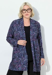 Cardigan lungo aperto di colore blu navy con stampa paisley in rosa e bianco. Tessuto morbido con maniche lunghe, indossato sopra una maglia nera.