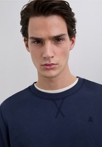 Navyblå sweatshirt med rund halsudskæring, ribbede ærmegab og et tekstureret design. Har et lille logo på brystet.