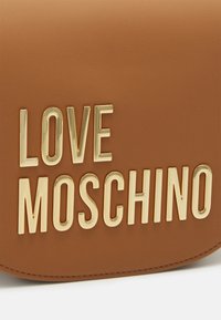 Borsa in finta pelle marrone con logo "LOVE MOSCHINO" in tono oro goffrato e in lettere bold. Texture liscia con bordi ricamati.